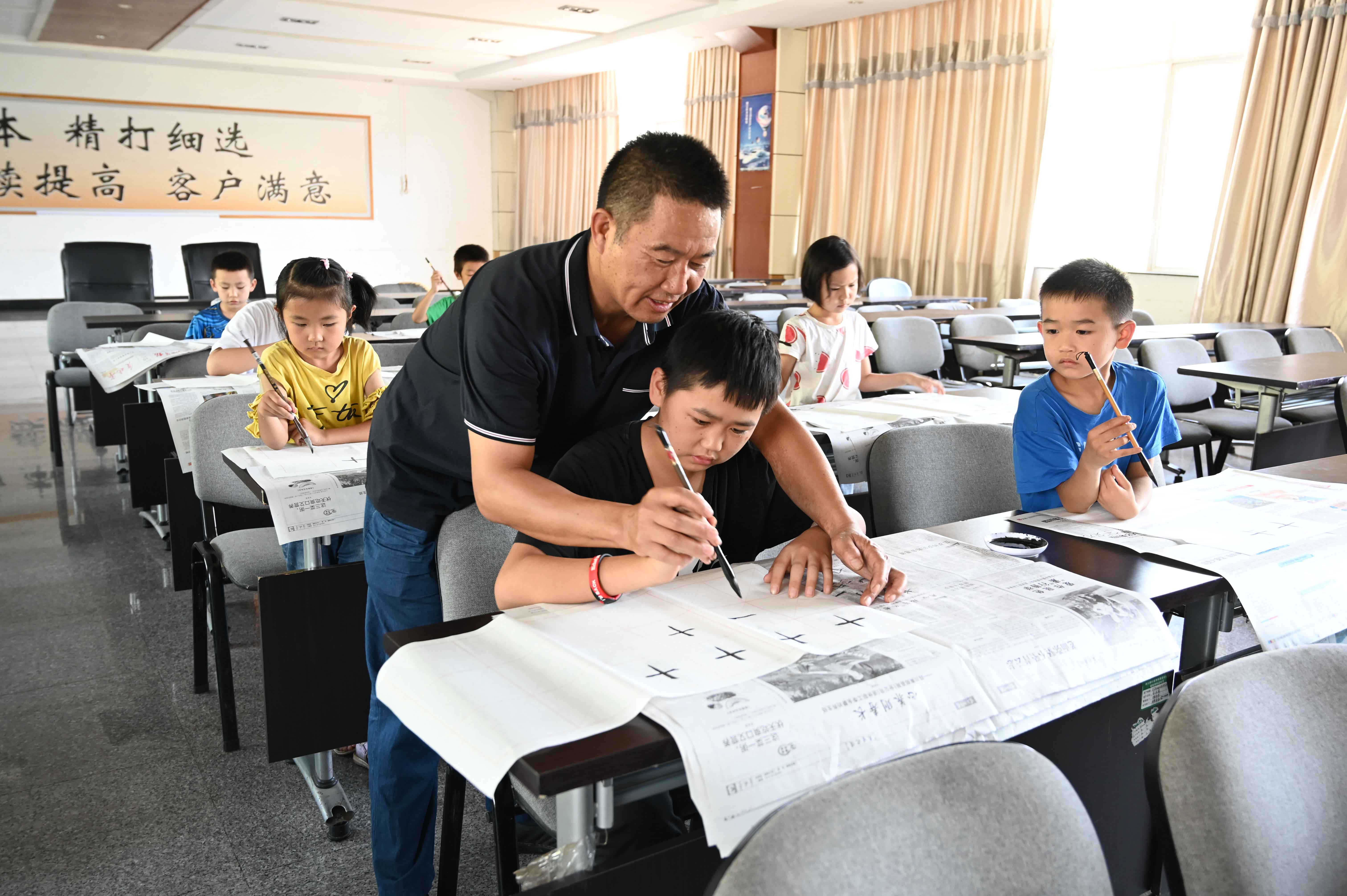 1721787155746846.jpg 托管班志愿老师正在教育孩童书法.JPG