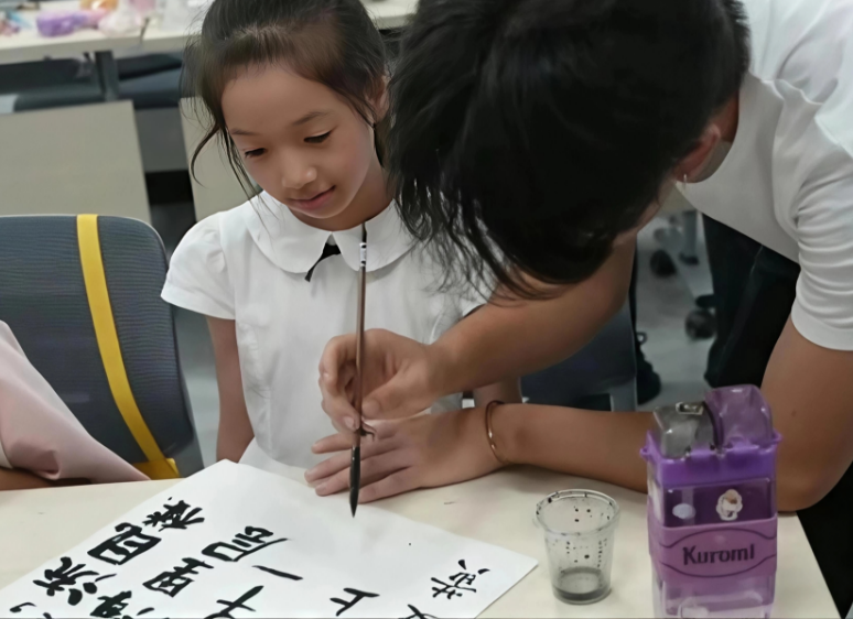 1753429385775011.png 志愿者教儿童们用毛笔书写古诗词.png